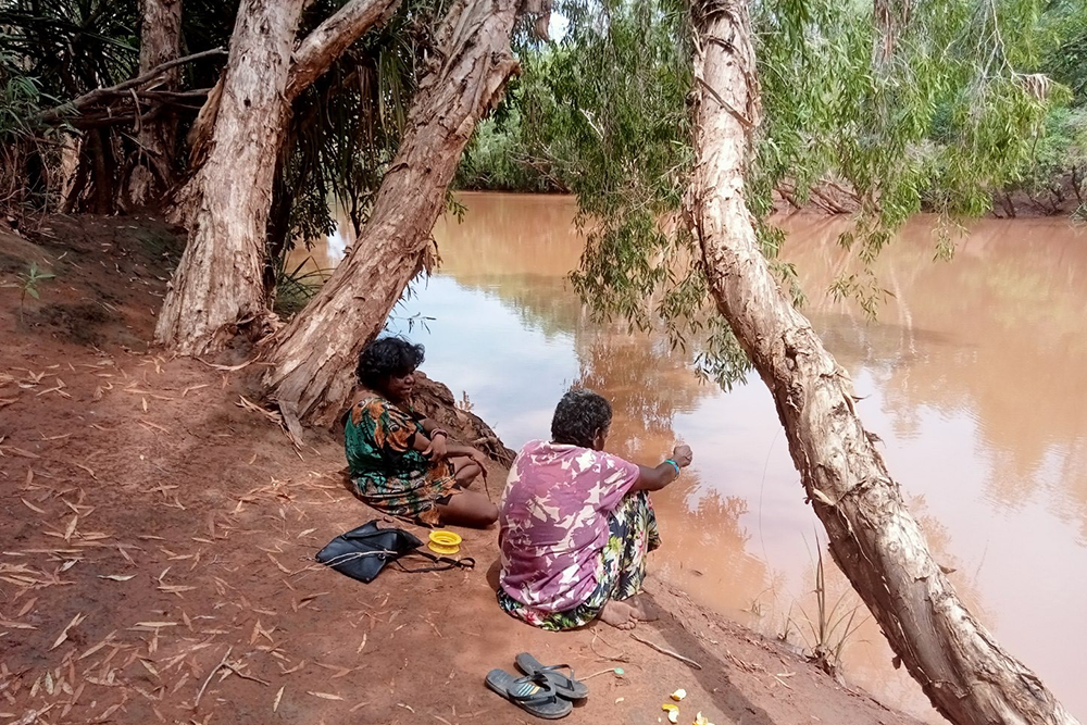 two women sitting by river fishing